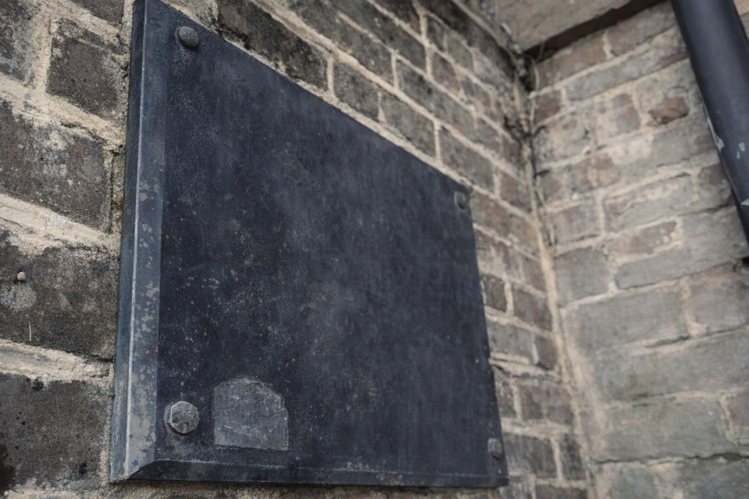 En mörk, tom metallskylt monterad på en rustik tegelvägg utomhus.